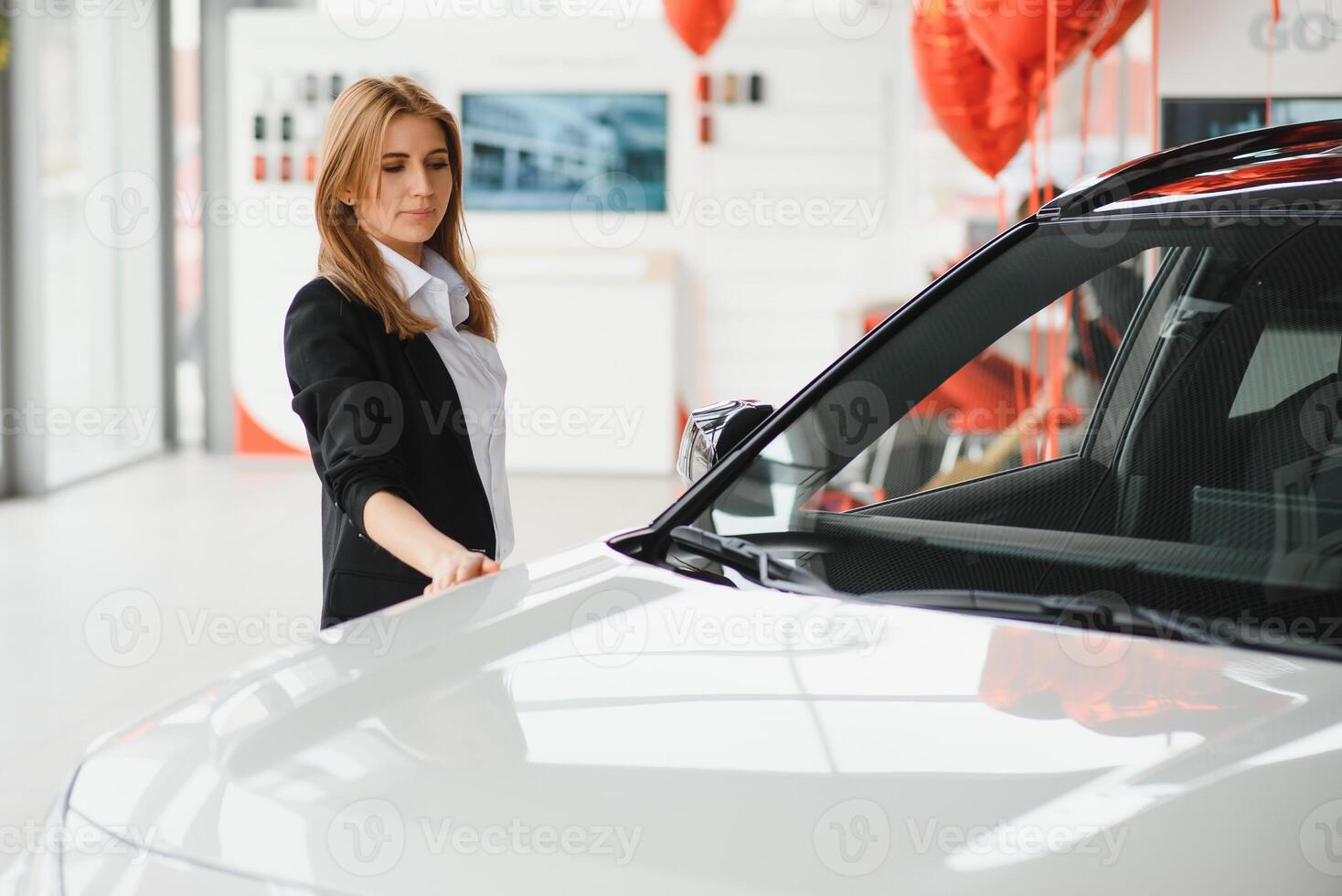 Young beautiful woman showing her love to a car in a car showroom. photo