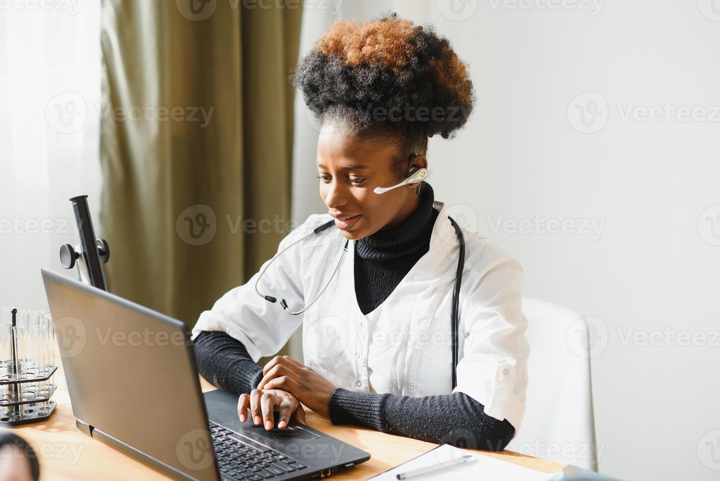 Smiling african american female doctor gp wears white medical coat using laptop computer at workplace gives remote online consultation, working on pc, consulting patient in internet telemedicine chat photo