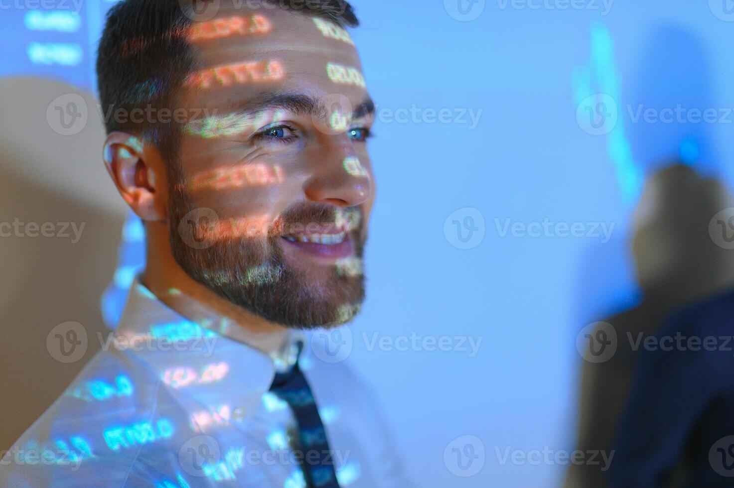 Stock Market Top Trader Looks at Projected Ticker Numbers and Graphs Running, Analysing Data to Make Best Sell. Behind Him Room Full of Screens and Statistics. photo