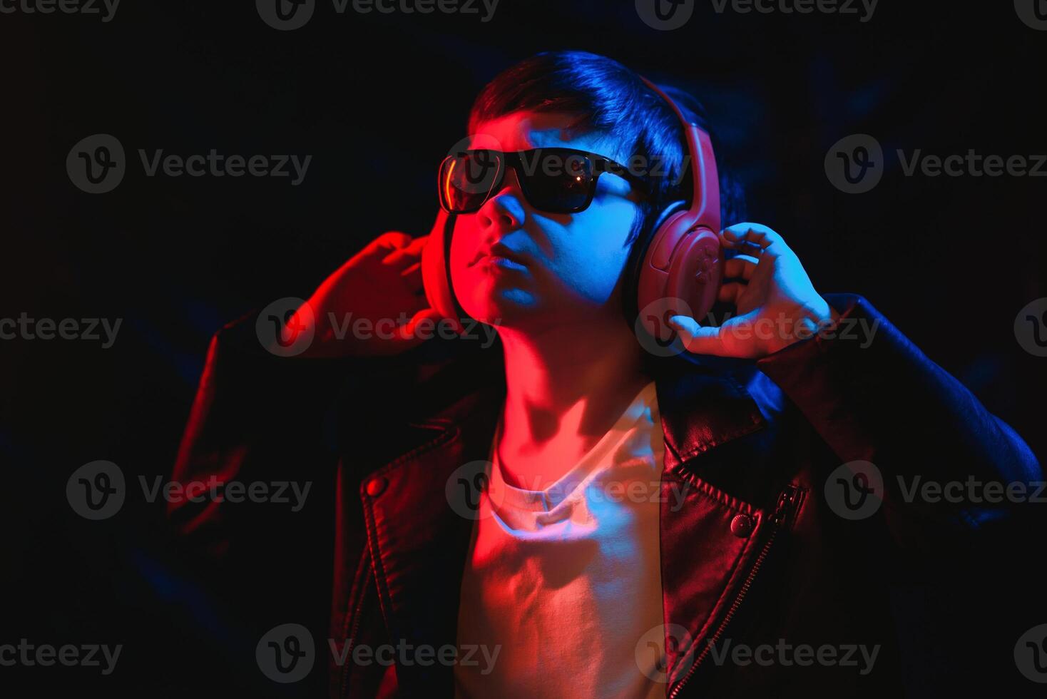 Studio shot in dark studio with neon light. Portrait of a stylish boy with headphones photo