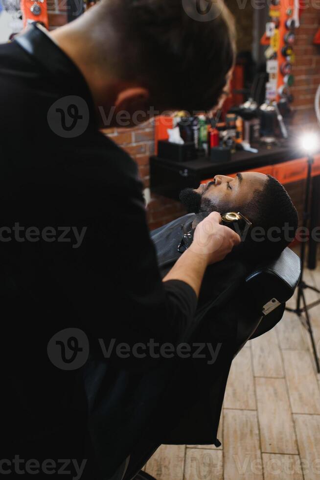 A barber is going through the electric cutting and shaving machine for the beard of an African-American Brazilian boy. photo