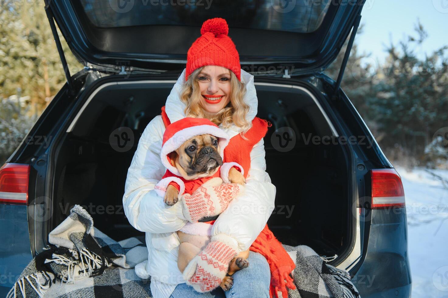 Woman resting in the winter forest sitting in the open trunk of a car with a dog. photo