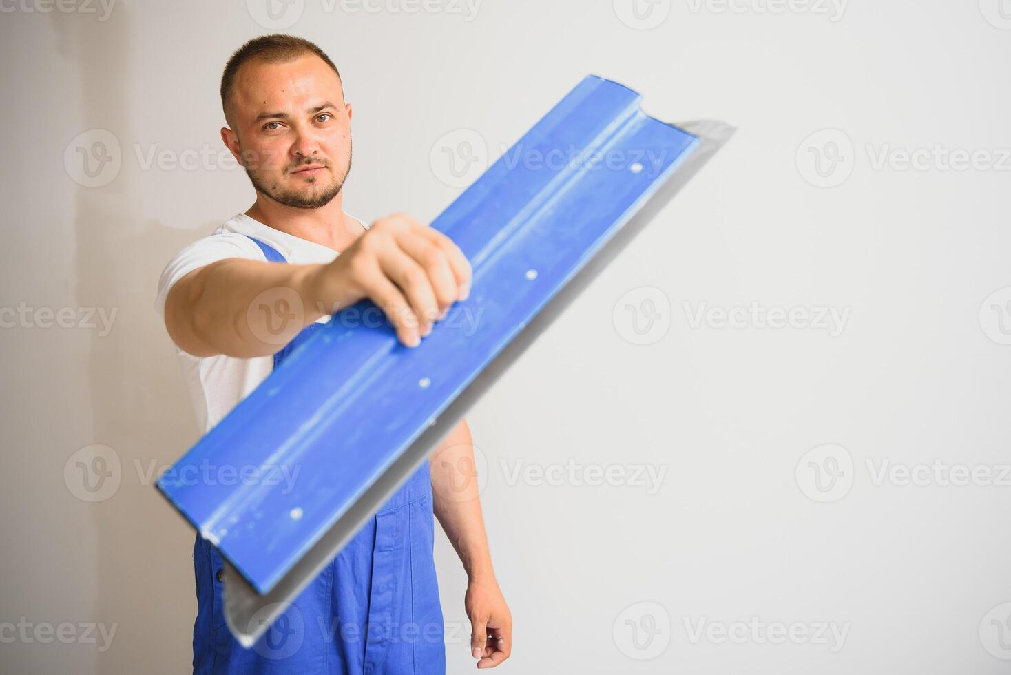 A general laborer in overalls uses a trowel to cover the wall with cement photo