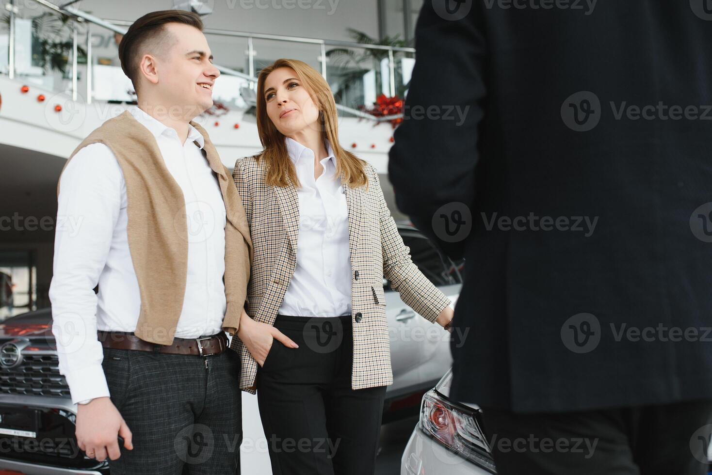 maduro vendedor demostración nuevo coche a un Pareja en sala de exposición. foto