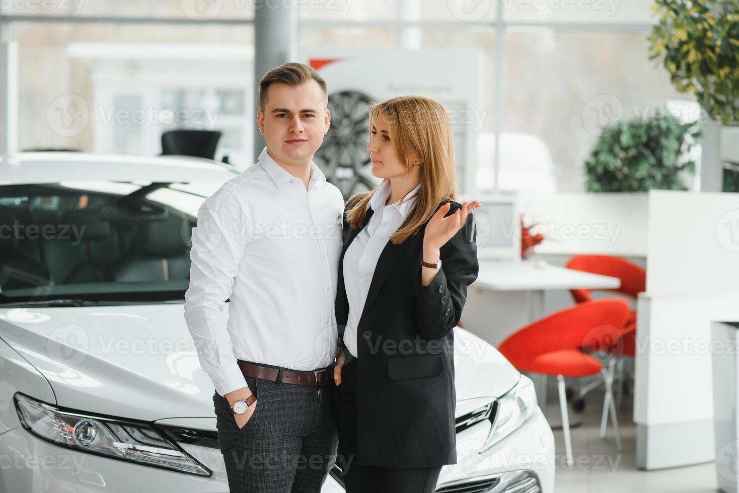 Young beautiful happy couple buying a car. Husband buying car for his wife in a salon. Car shopping concept photo