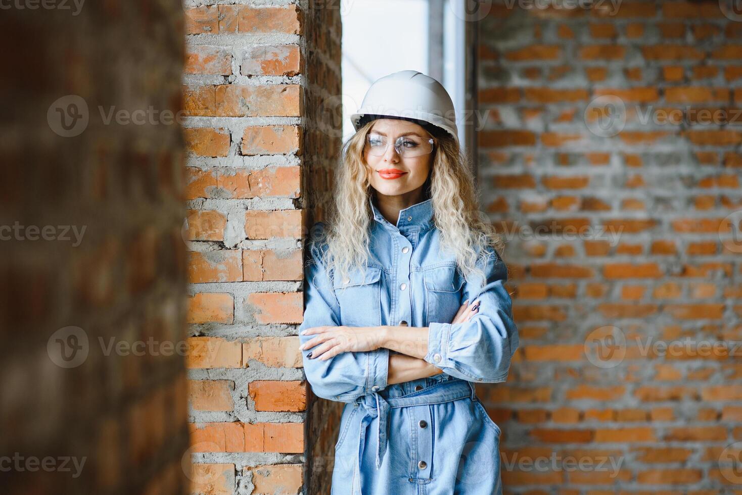 atractivo hembra construcción trabajador en casco de seguridad. confidente joven especialista en a cuadros azul camisa en pantalones en pie en vacío habitación. interior diseño y renovación servicio. foto