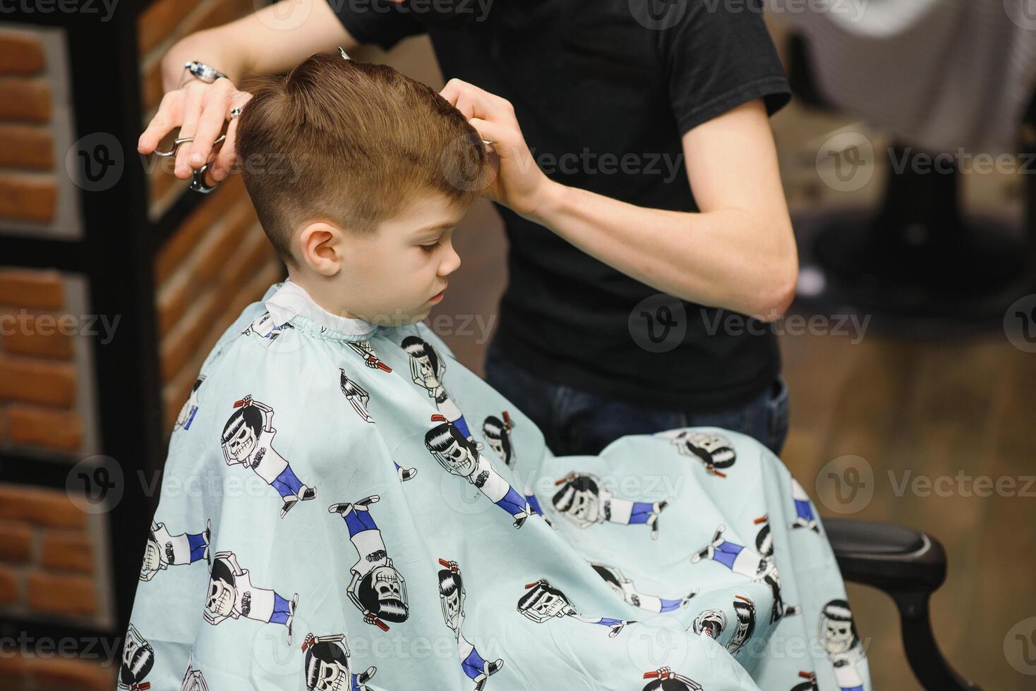 Side view of cute little boy getting haircut by hairdresser at the barbershop. photo