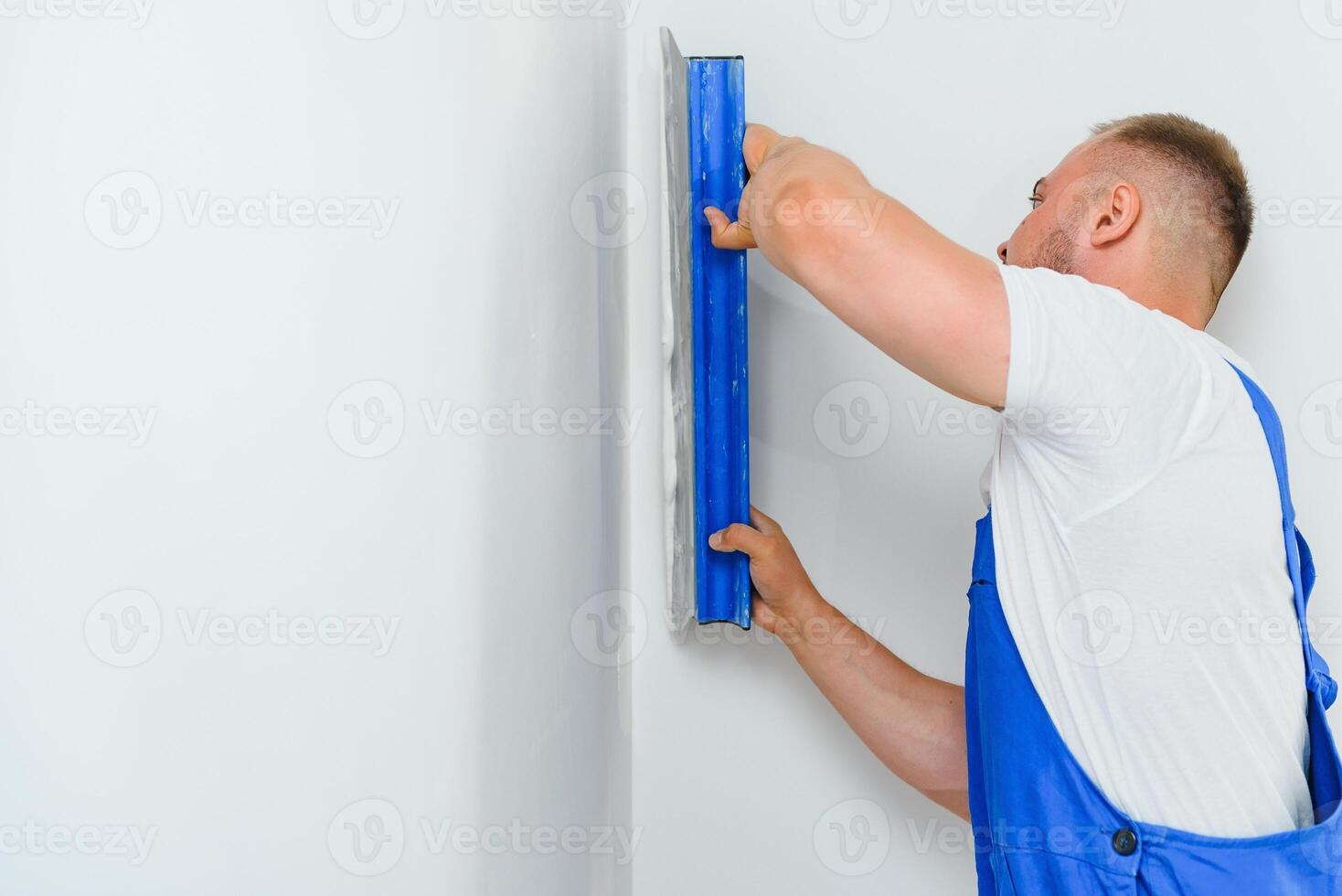 A general laborer in overalls uses a trowel to cover the wall with cement photo