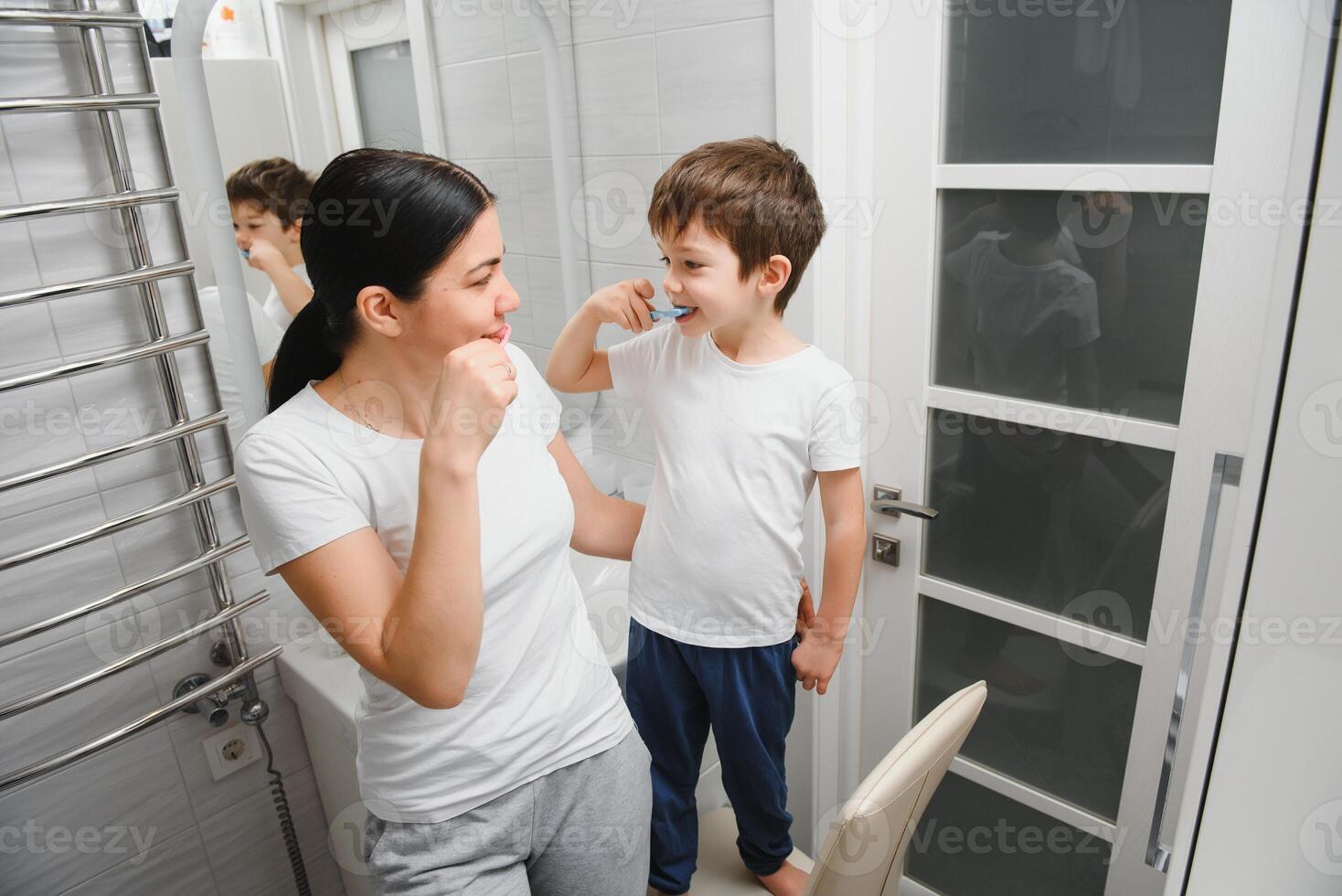 Beautiful mother and happy son brushing teeth near mirror in bathroom photo