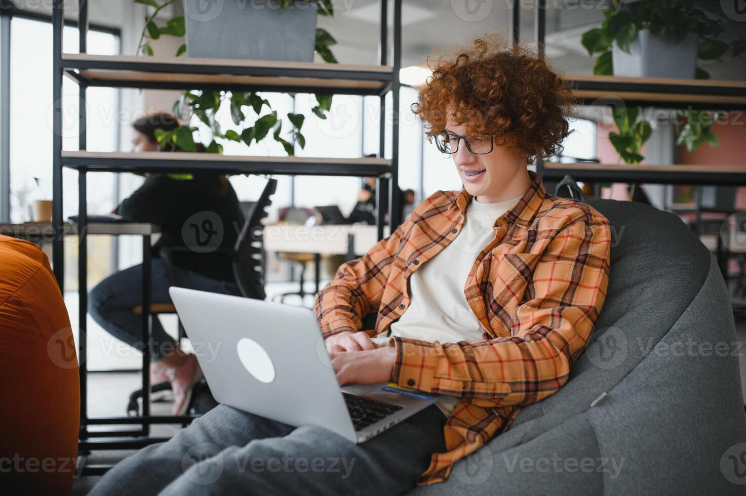Portrait of Caucasian male freelancer in trendy apparel sitting at cafeteria table and doing remote work for programming design of public website, skilled software developer posing in coworking space. photo