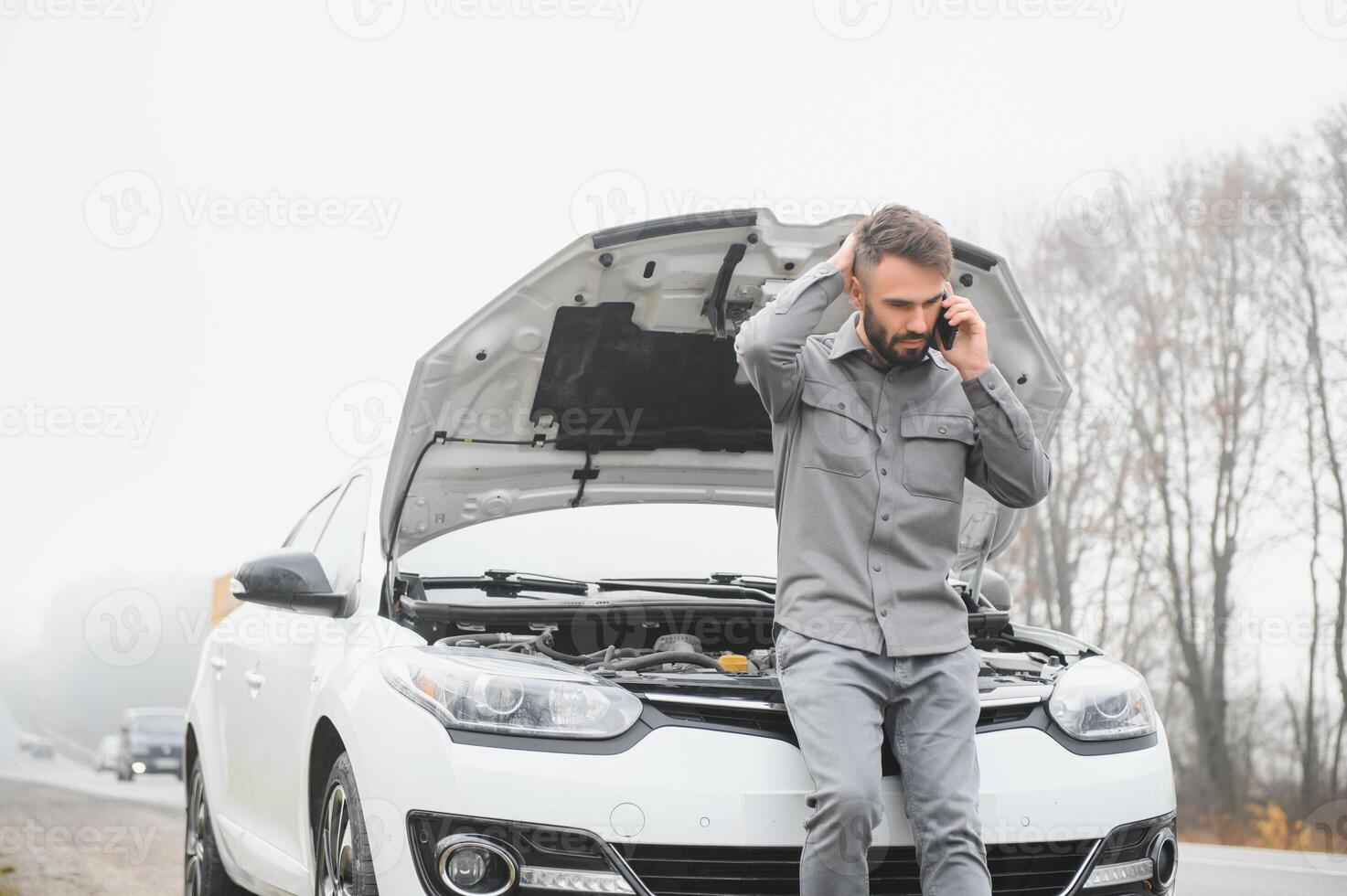 Sad driver calling car service, opening hood, having engine problem standing near broken car on the road. Car breakdown concept photo