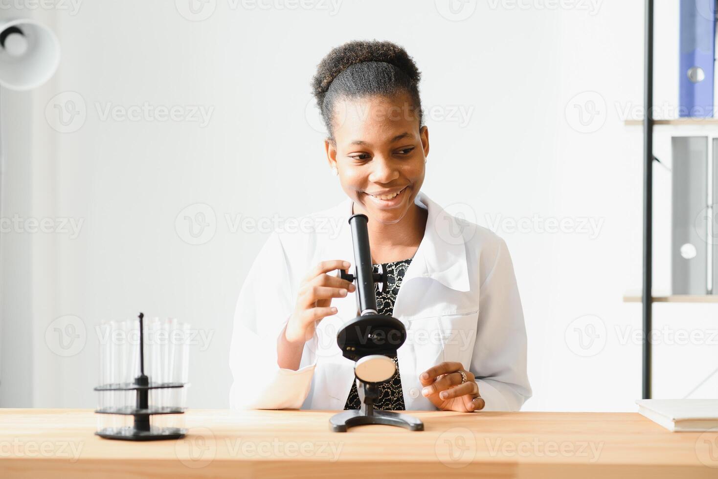 african american female lab technician looking through microscope in lab. photo