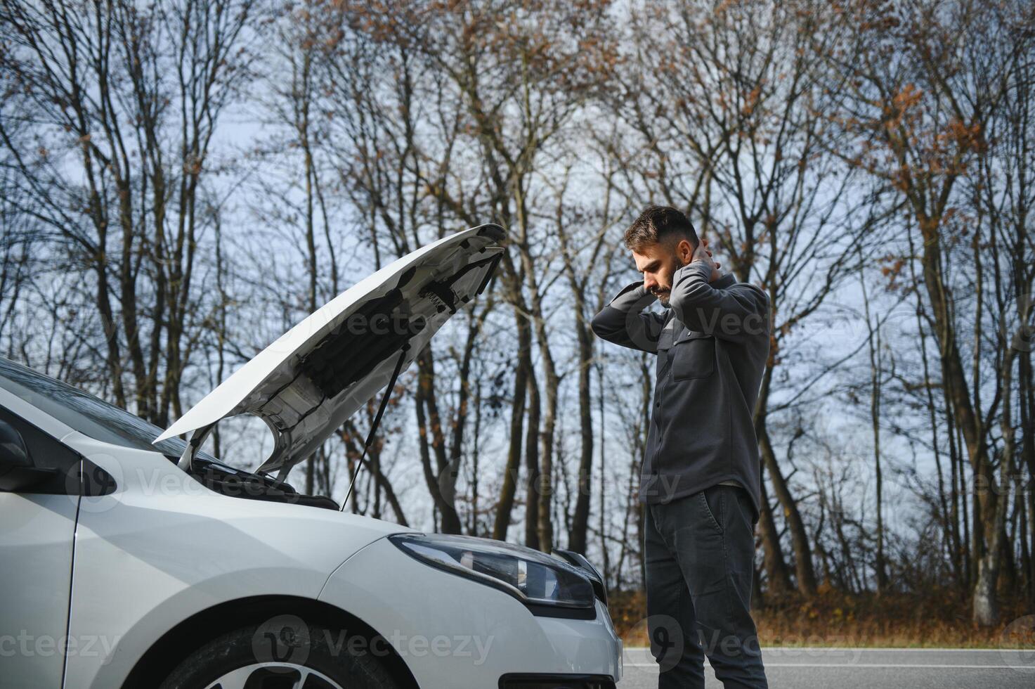 Sad driver holding his head having engine problem standing near broken car on the road. Car breakdown concept photo