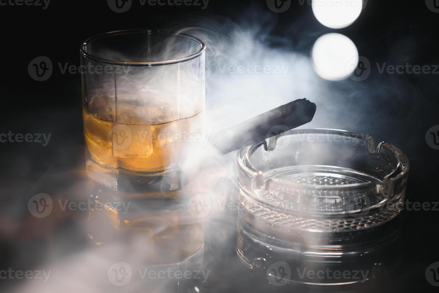 Glass of whiskey with ice cubes and smoking cigar on table photo