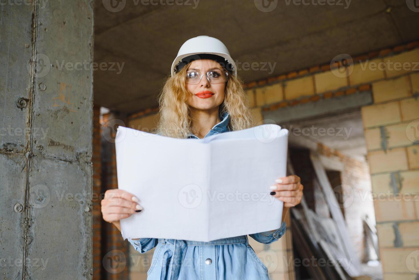 Construction concept. Pretty female builder in overalls and helmet working on construction site. photo