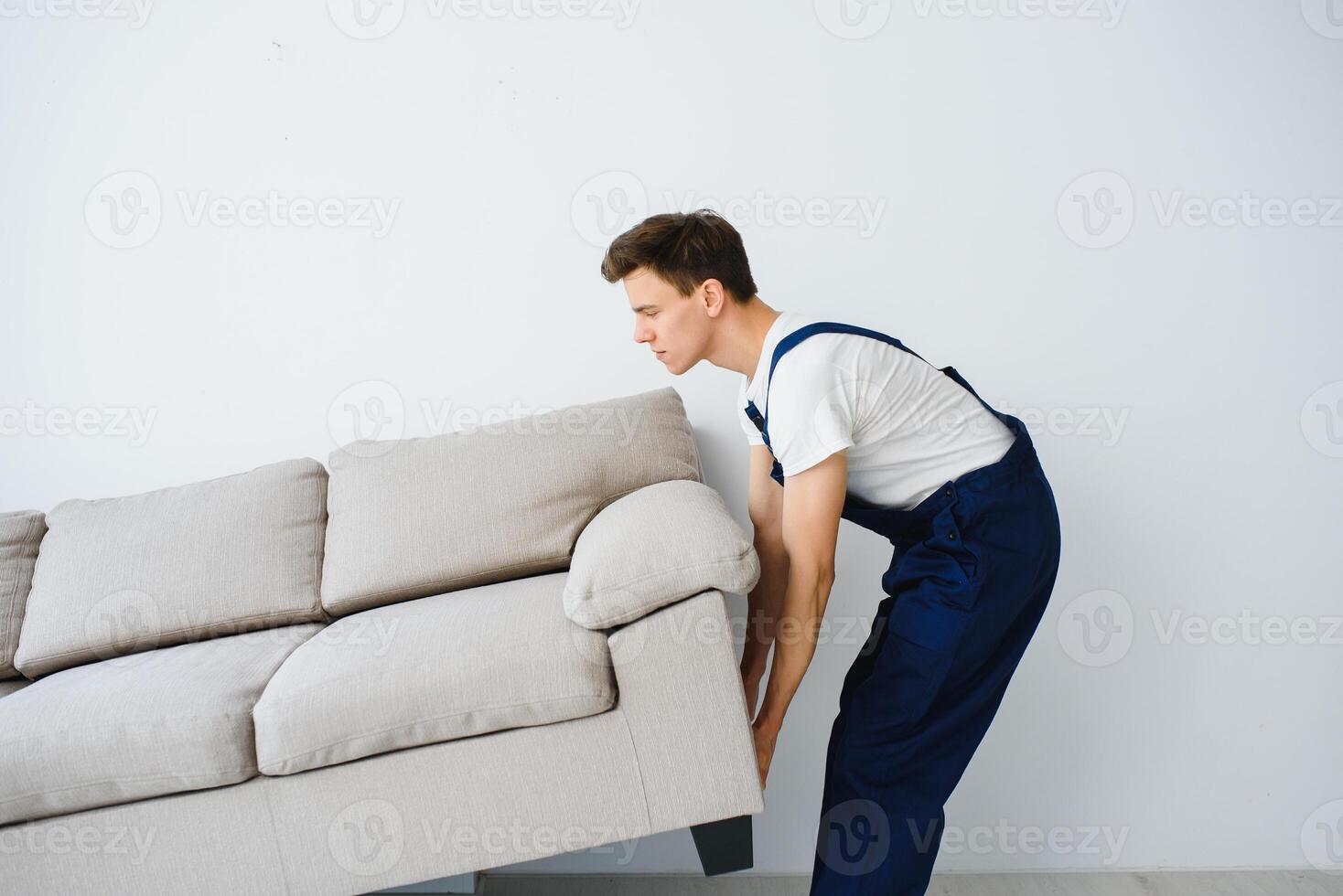 Loader moves sofa, couch. worker in overalls lifts up sofa, white background. Delivery service concept. Courier delivers furniture in case of move out, relocation. photo