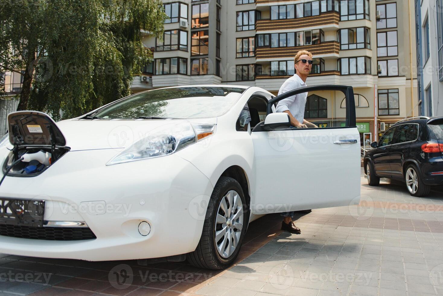 linda joven hombre cerca un moderno eléctrico coche. el concepto de ecológico transporte. foto