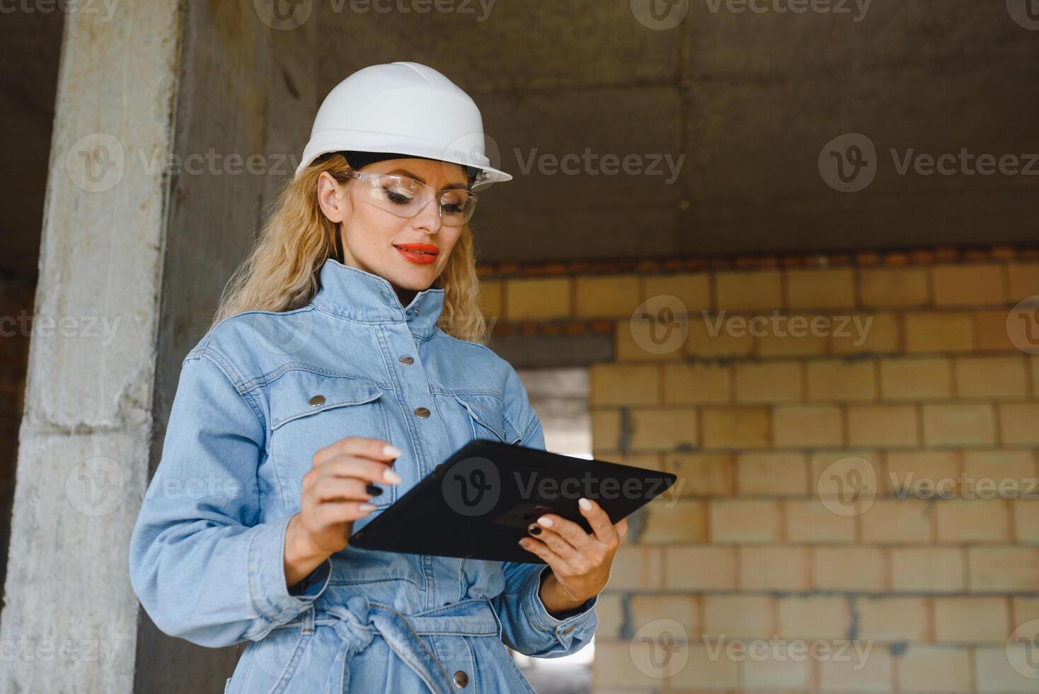 Construction concept. Pretty female builder in overalls and helmet working on construction site. photo