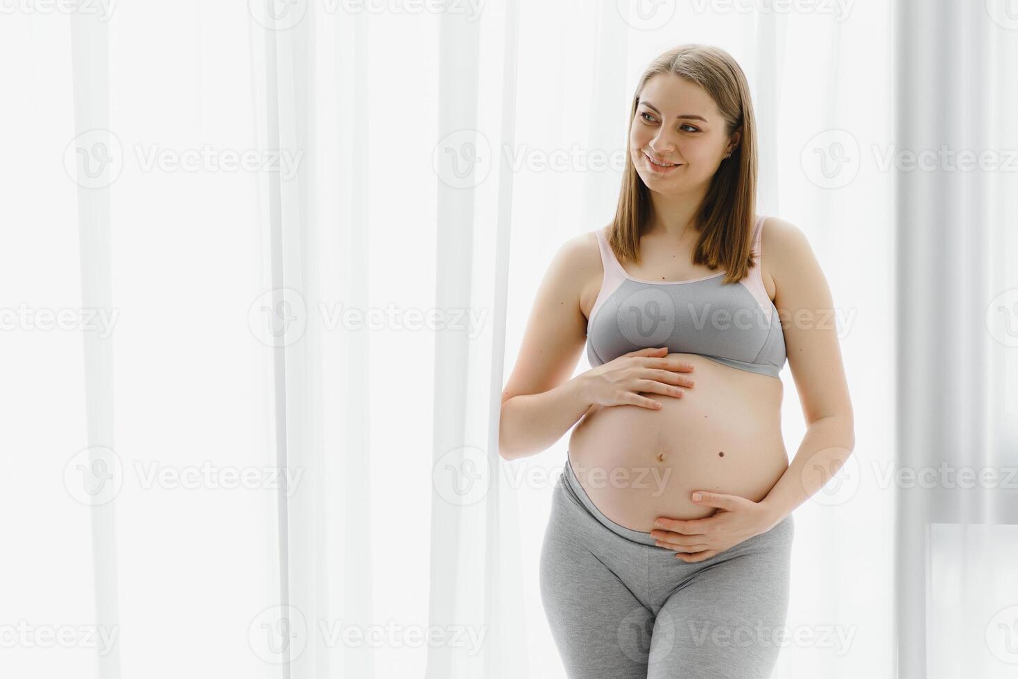 Young beautiful pregnant woman standing at home near the window. photo