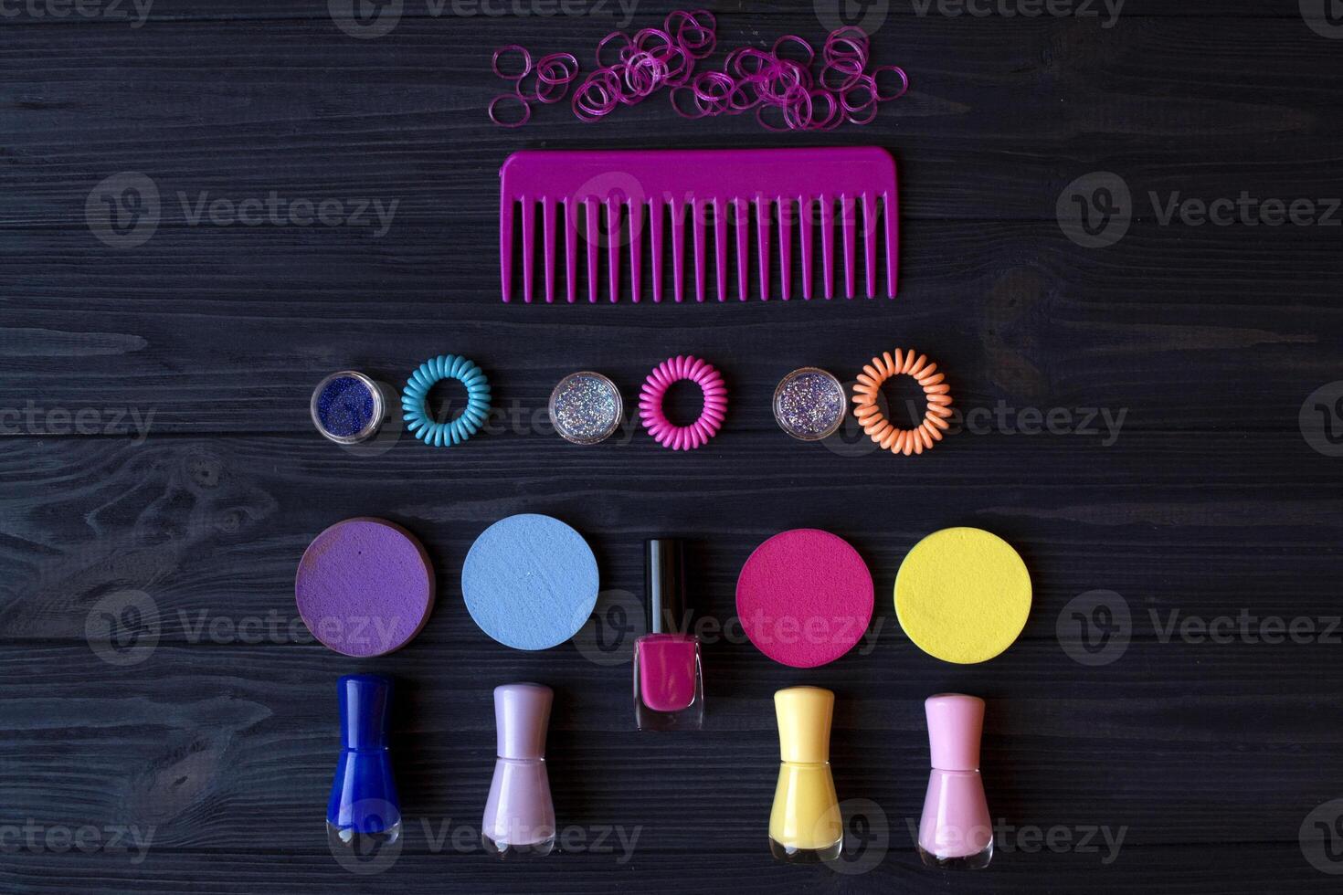 Colorful and bright cosmetics. Beauty care tools. Beauty salon. Girl's paradise. Nail polishes, sequins, pink hair bands and comb on a dark blue wooden desk. Bright still life of beauty instruments. photo