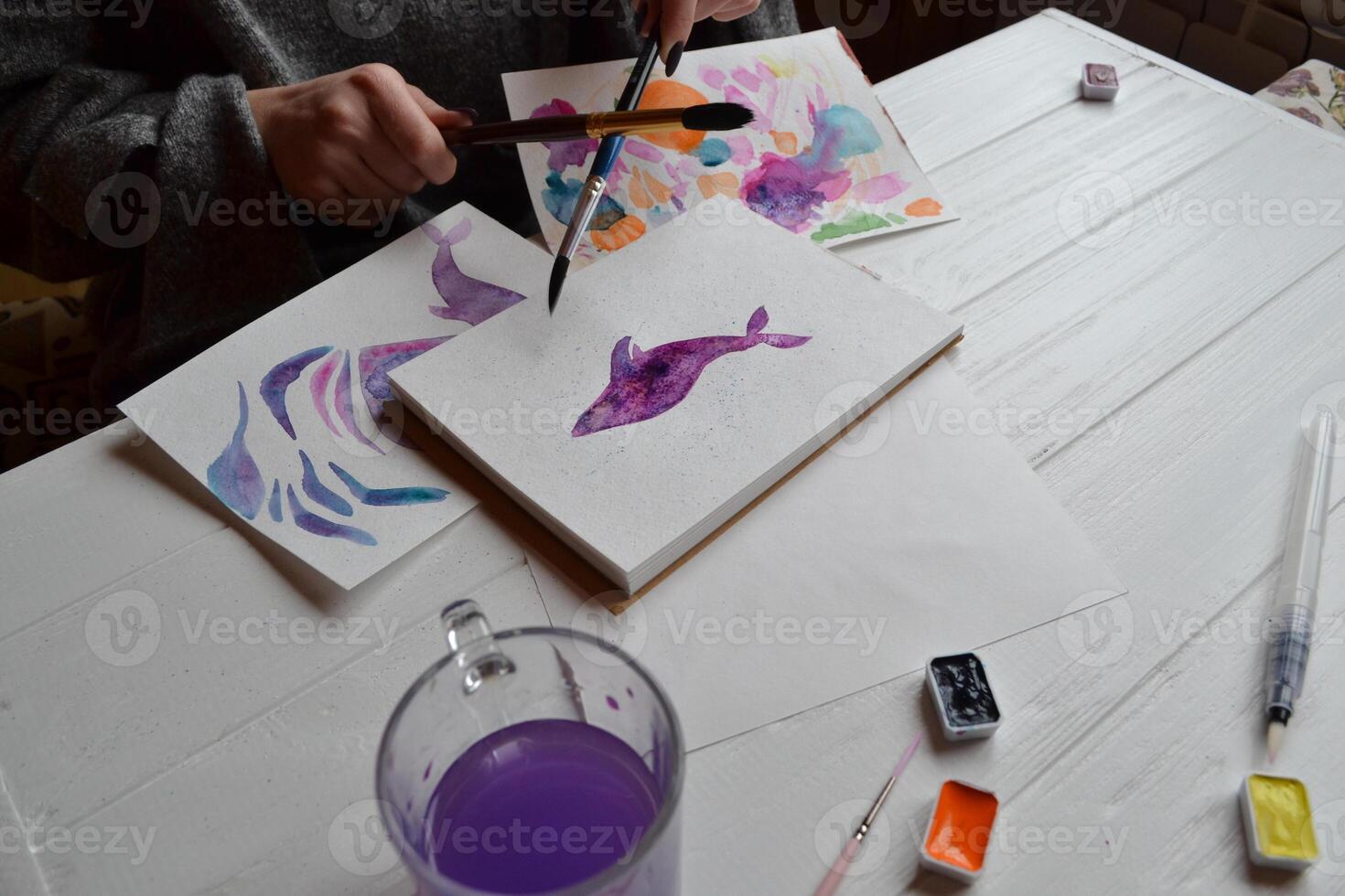 Woman paints in a sketchbook. Tools for painting on the white wooden desk. Painter work. photo