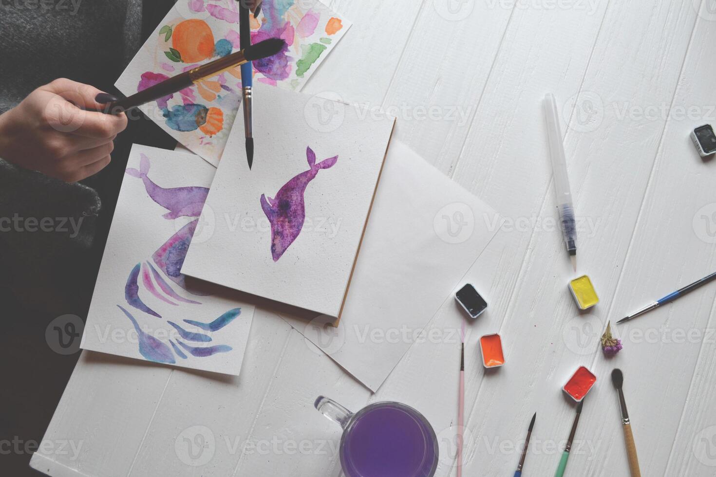 Woman paints in a sketchbook. Tools for painting on the white wooden desk. Painter work. photo