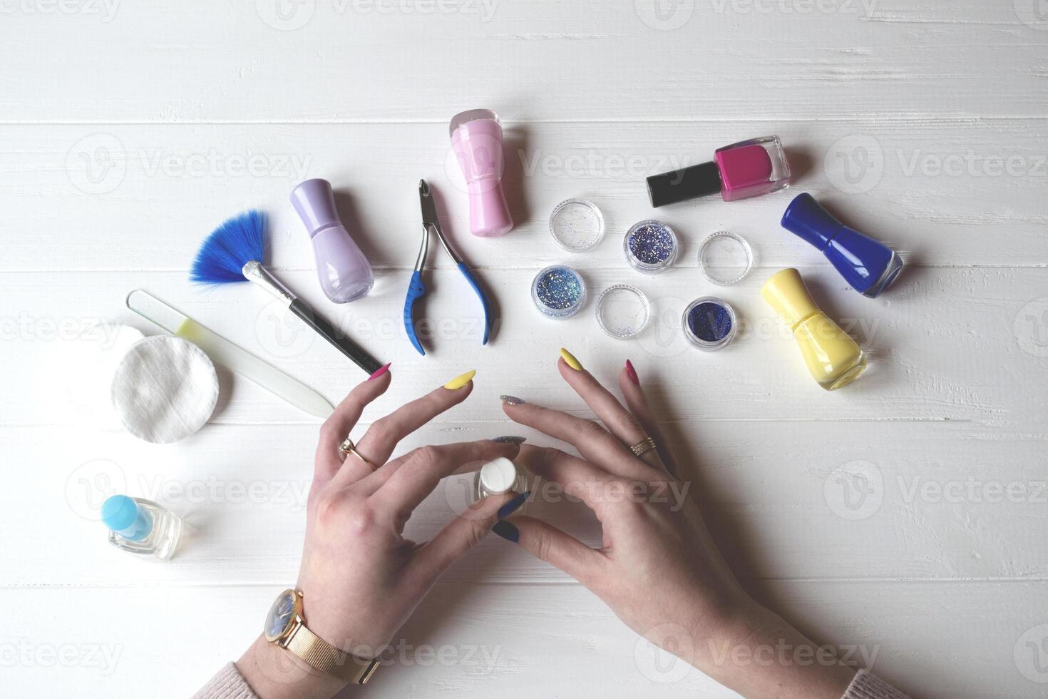 A woman painting her nails. Tools for manicure on a white wooden table. photo