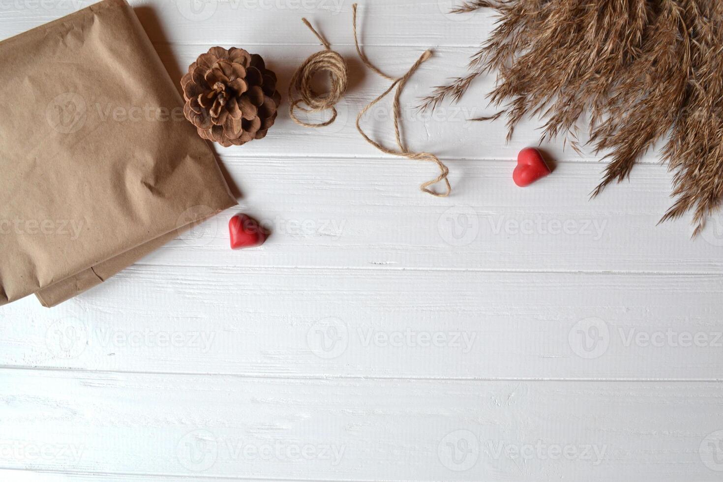 Craft paper, notebook, red hearts, rope and natural objects on the white wooden desk. Gift wrapping. Valentine's Day. Background with place for text. photo