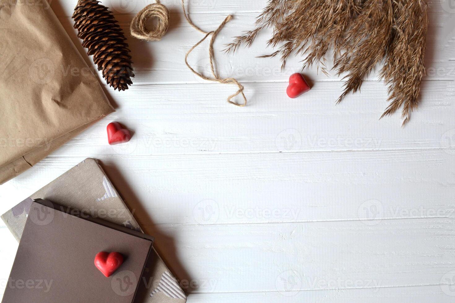 Craft paper, notebook, red hearts, rope and natural objects on the white wooden desk. Gift wrapping. Valentine's Day. Background with place for text. photo