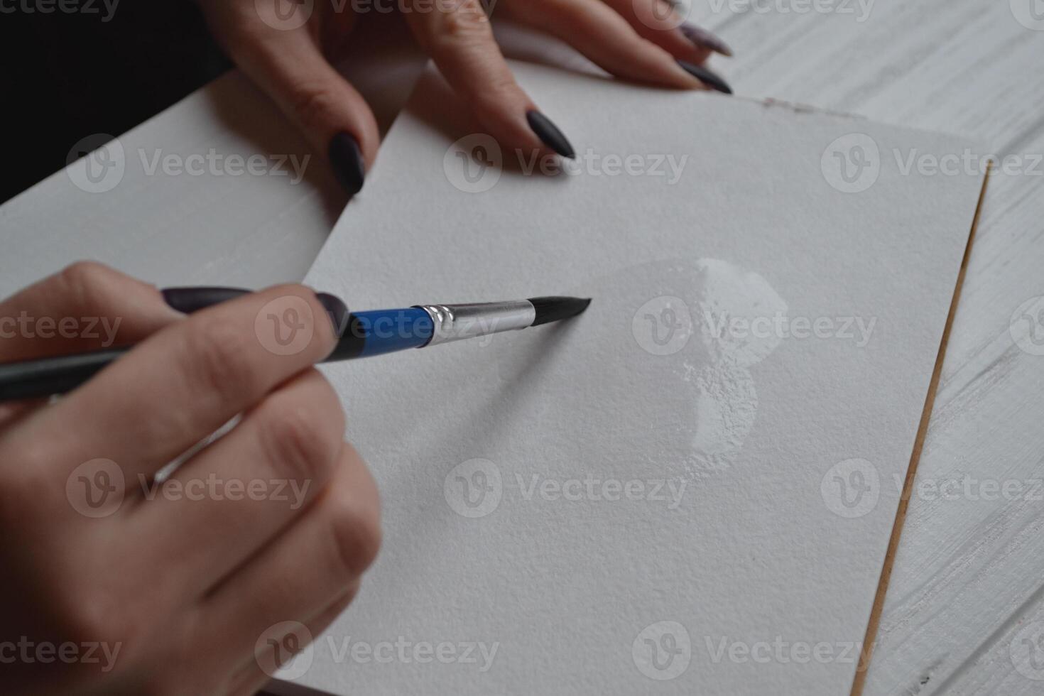 Woman paints in a sketchbook. Tools for painting on the white wooden desk. Painter work. photo