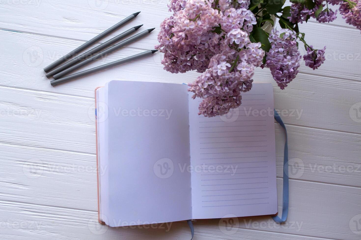 abrió computadora portátil, gris lapices y lila en florero en un blanco de madera escritorio. foto