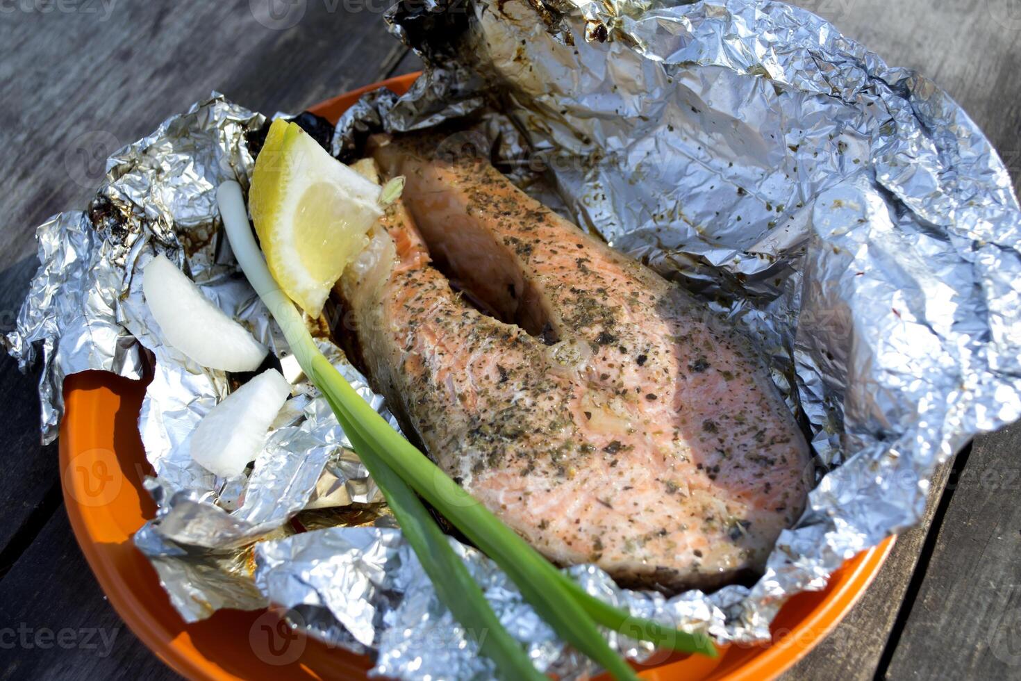 A trout cooked at the stake in orange plate on a wooden table outdoor. photo