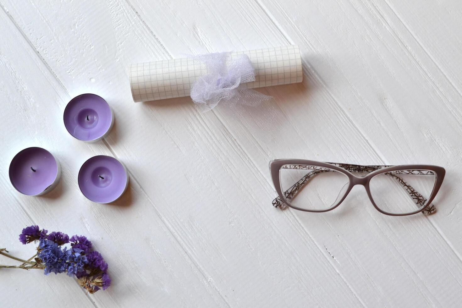 Letter, glasses, candle and flower on the white table. Beutiful female objects on the white wooden background. Flat lay in violet color. photo