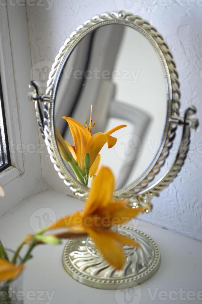 The orange lily near mirror. Flowers and mirror reflection. photo