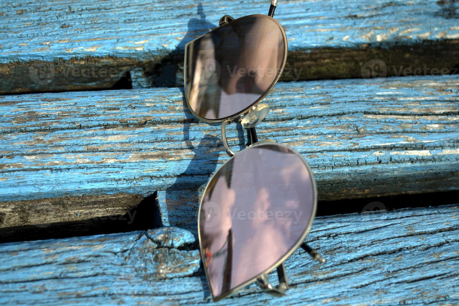 Sunglasses on a blue wooden backgorund. The sky is reflected in sunglasses. photo