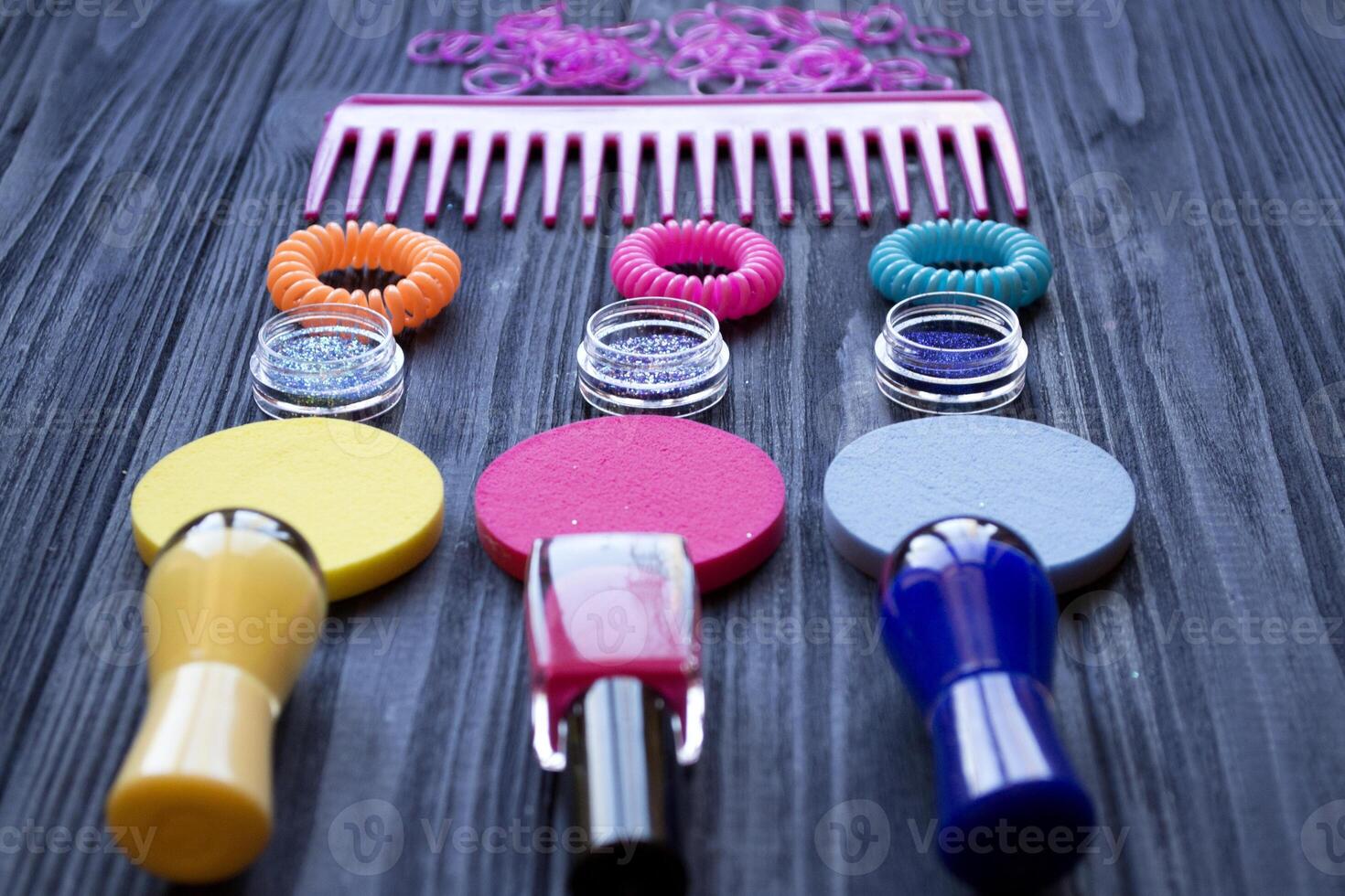 Colorful and bright cosmetics. Beauty care tools. Beauty salon. Girl's paradise. Nail polishes, sequins, pink hair bands and comb on a dark blue wooden desk. Bright still life of beauty instruments. photo