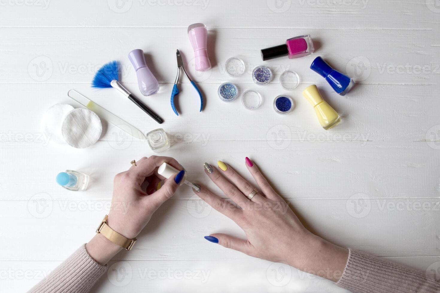 A woman painting her nails. Tools for manicure on a white wooden table. photo
