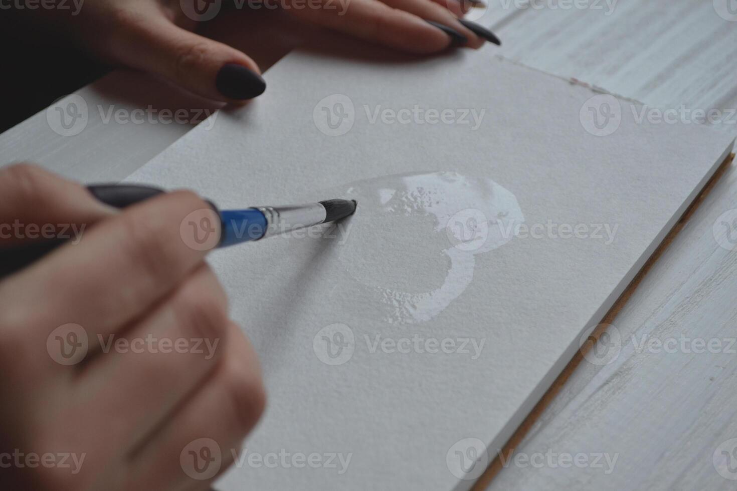 Woman paints in a sketchbook. Tools for painting on the white wooden desk. Painter work. photo