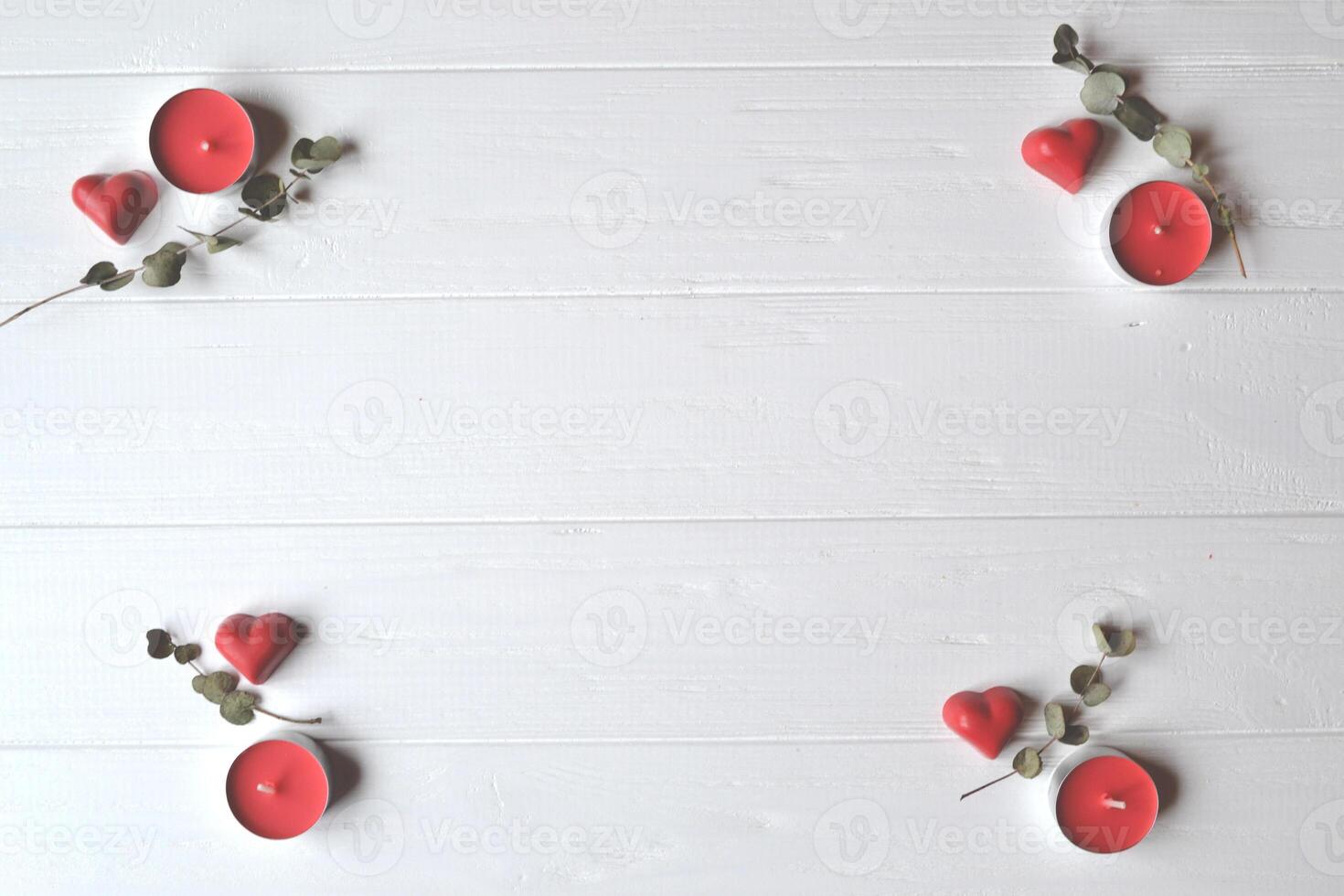 Red candies in a form of heart and red candles on the white wooden table. Background for greeting card on Valentine's day with place for text. photo