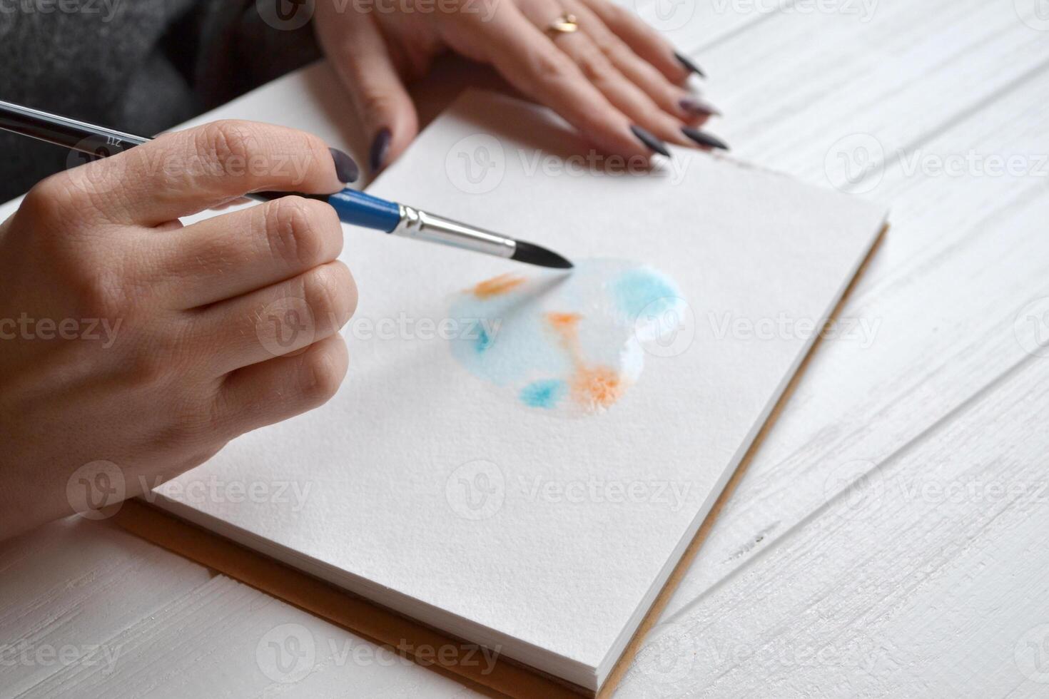 Woman paints in a sketchbook. Tools for painting on the white wooden desk. Painter work. photo