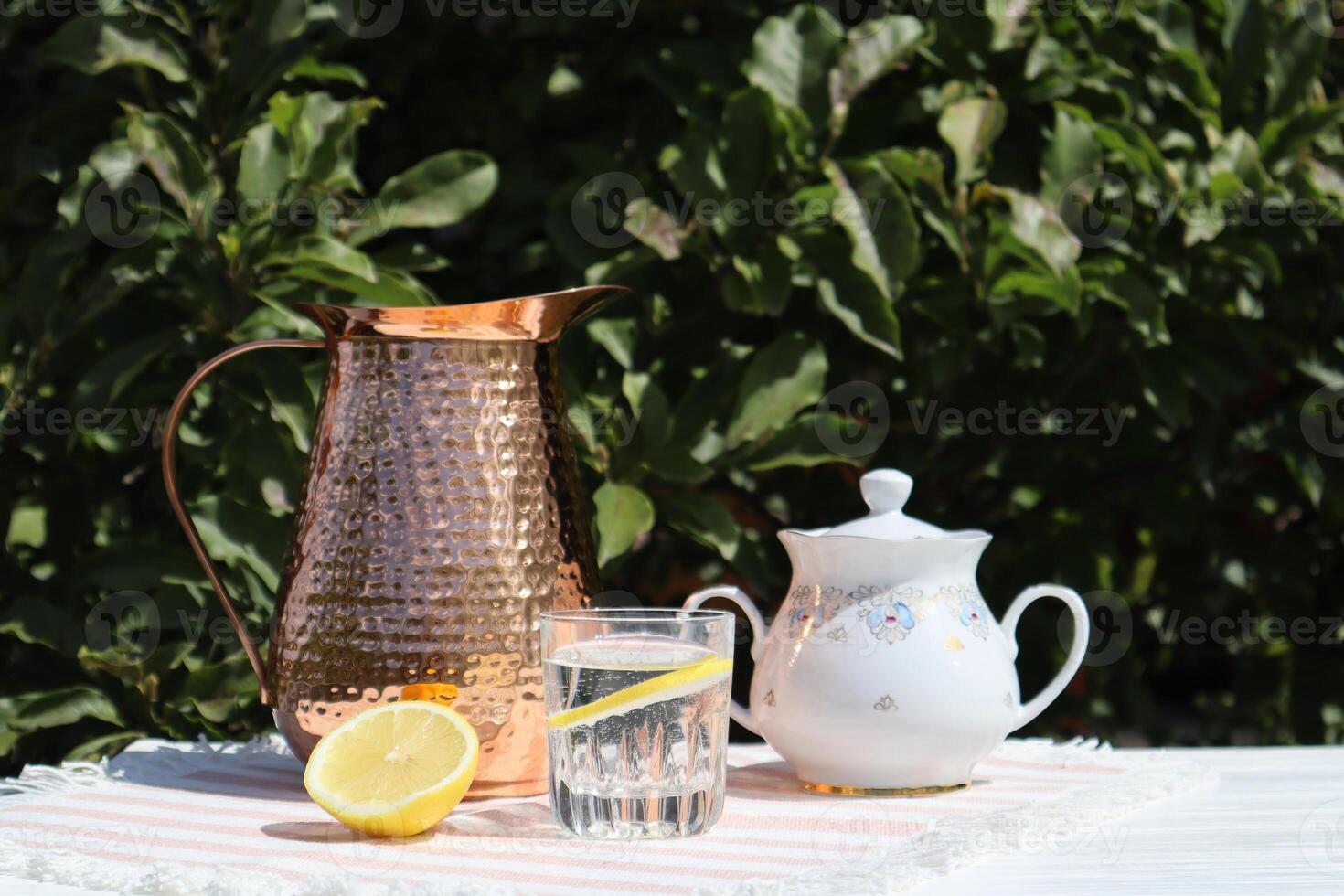 Copper pitcher and water with lemon on the wooden table outdoor. Summer still life with water and pitcher. photo