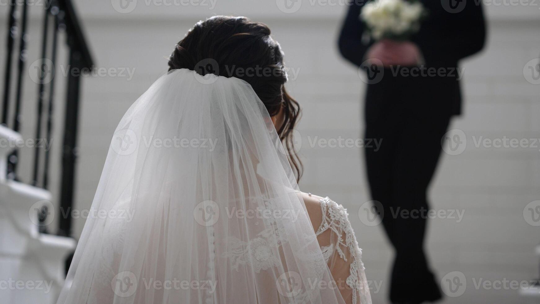 The groom approaches the bride with a bouquet. The bride stands with her back and the groom approaches her. The first meeting of the bride and groom. photo