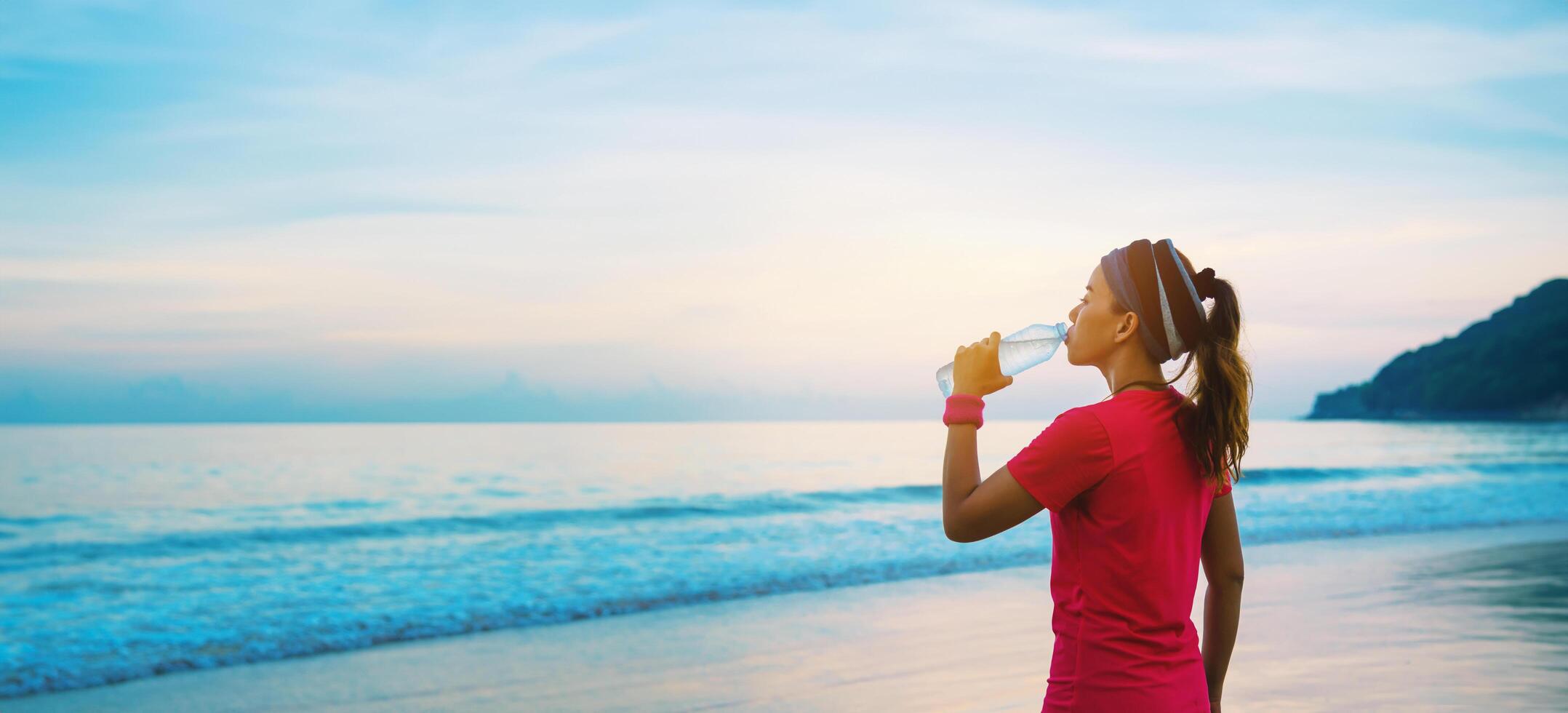 mujeres asiáticas jogging entrenamiento en la playa por la mañana. relájate con el paseo marítimo y bebe agua de las botellas de plástico foto