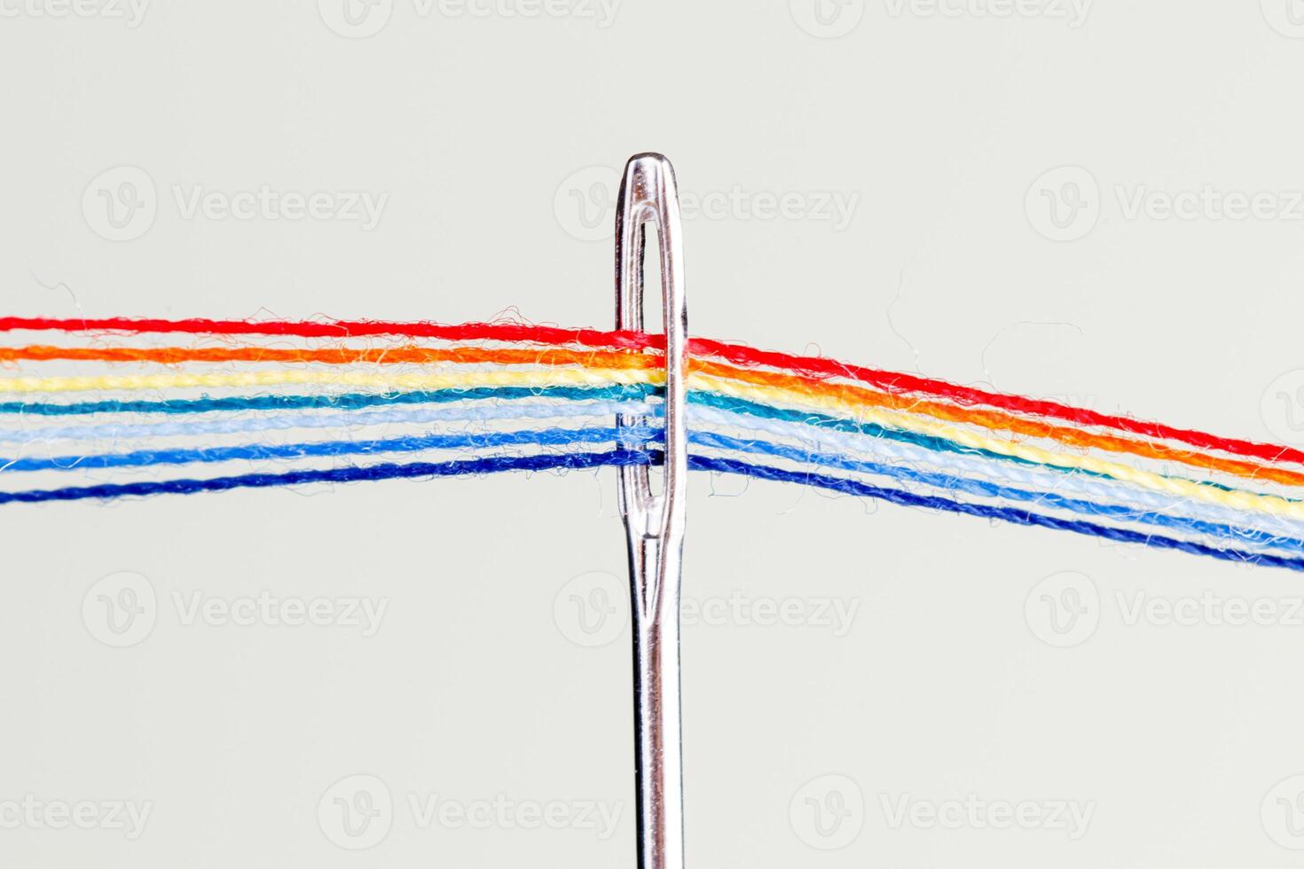 multi-colored threads for sewing in the form of a rainbow pass through an antique needle on a white background photo