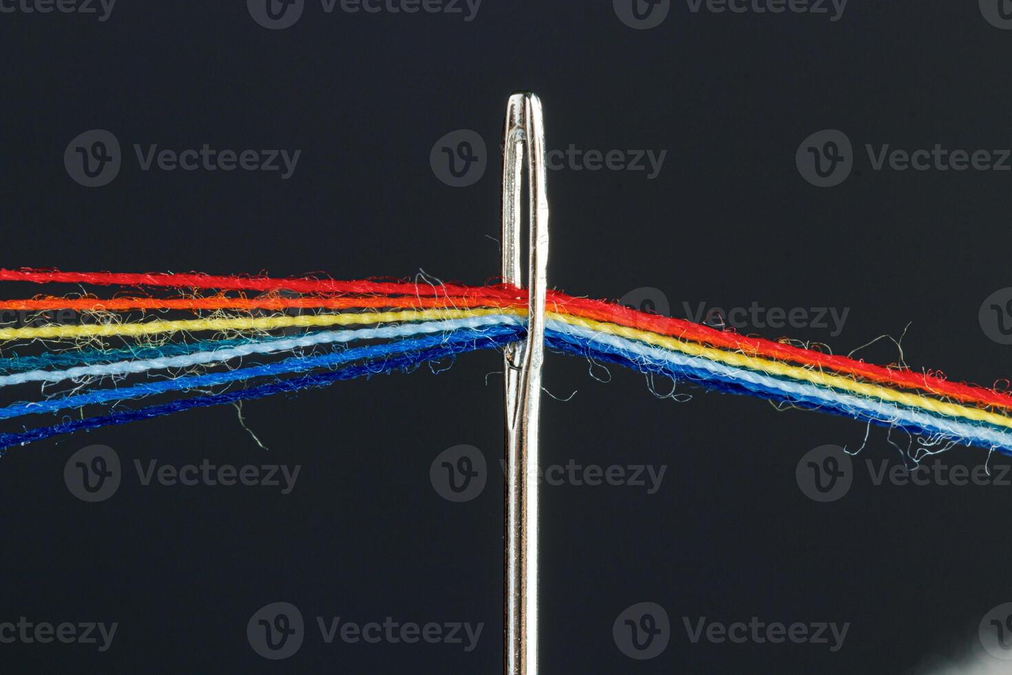 multi-colored threads for sewing in the form of a rainbow pass through an antique needle on a black background photo