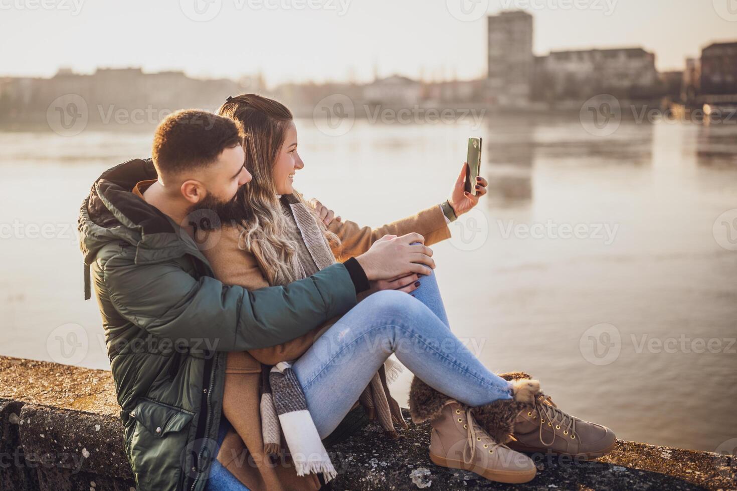 Happy couple photographing  cityscape with mobile phone  while spending time together by the river. photo