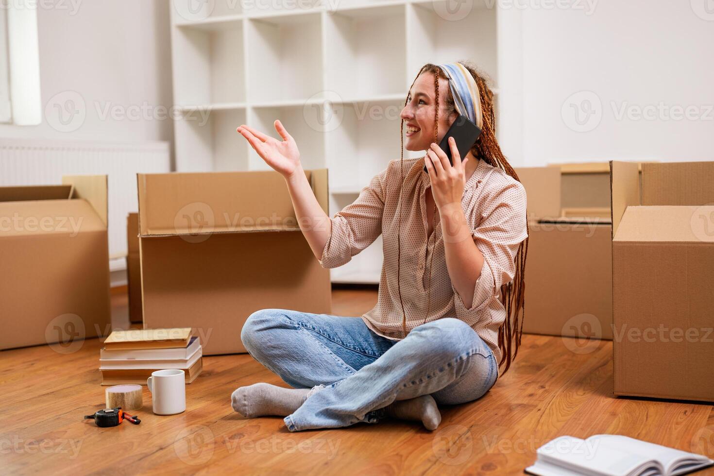 Modern ginger woman with braids talking on the phone while moving into her new apartment. photo