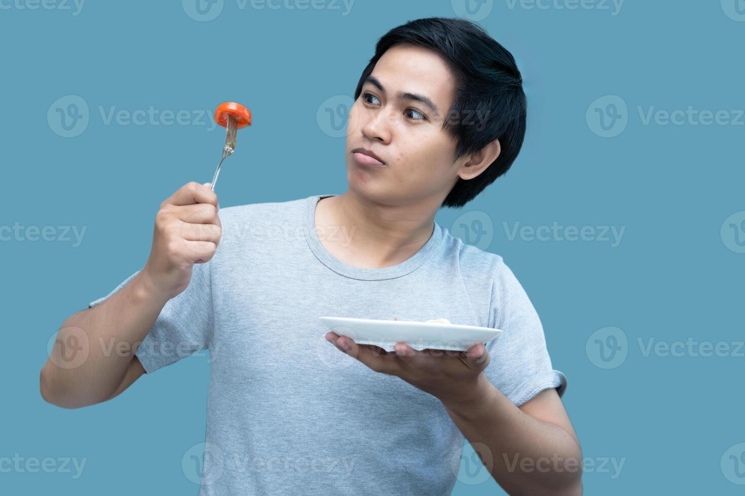 A man in a gray shirt is holding a fork and a plate containing food, for design and visual editing purposes. photo