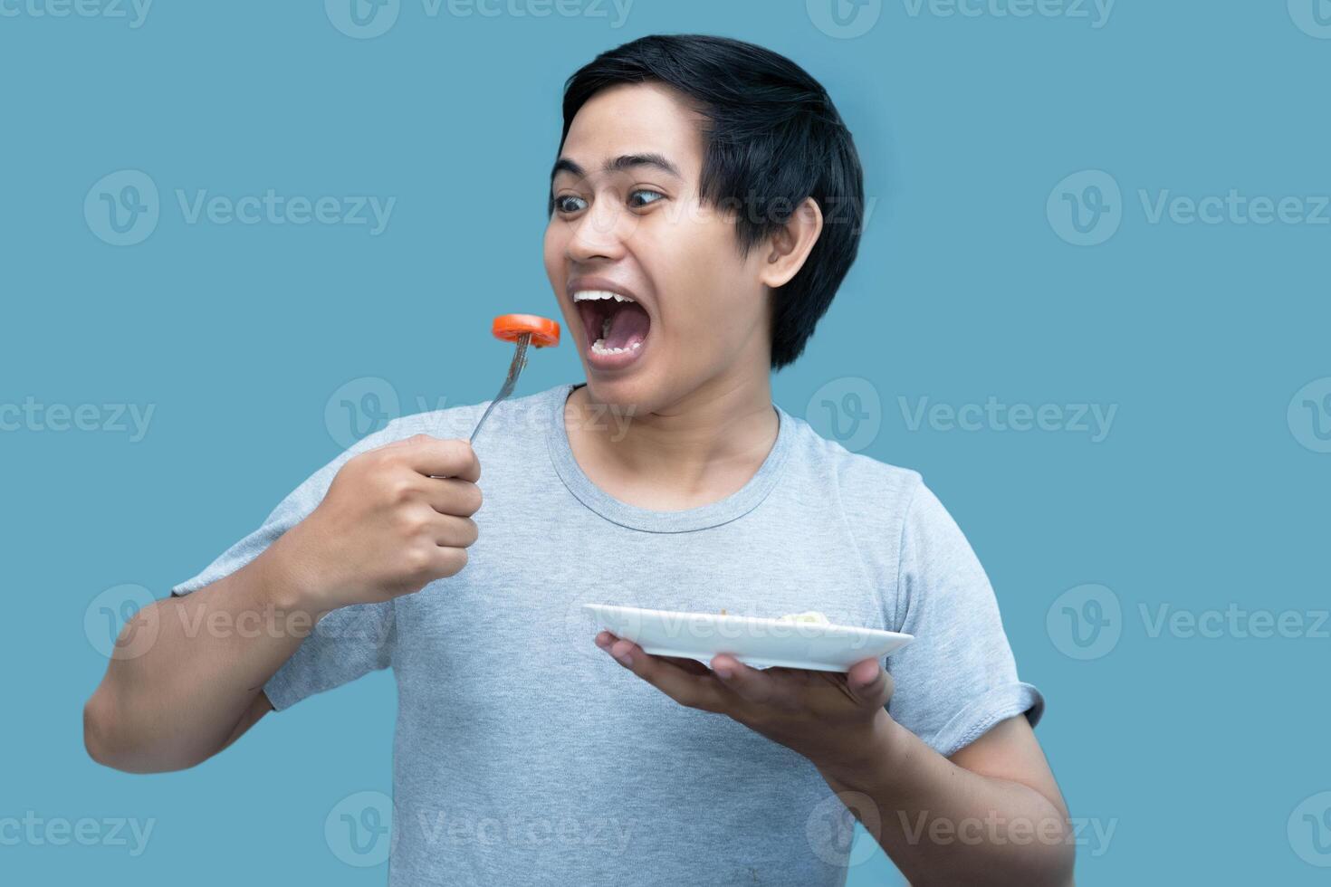 A man in a gray shirt is holding a fork and a plate containing food, for design and visual editing purposes. photo