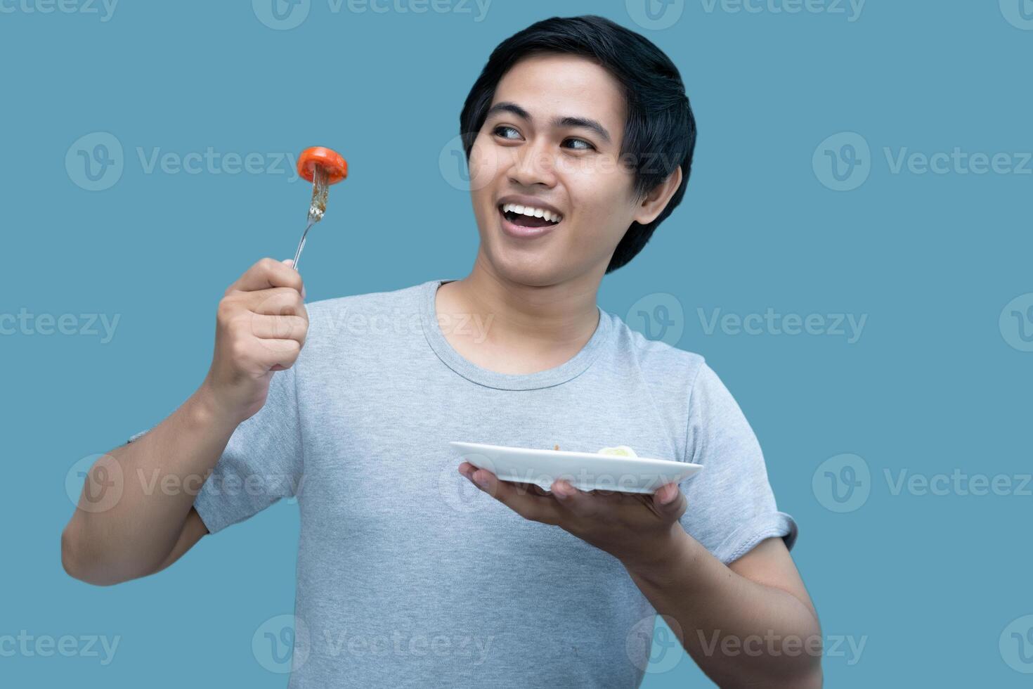 A man in a gray shirt is holding a fork and a plate containing food, for design and visual editing purposes. photo
